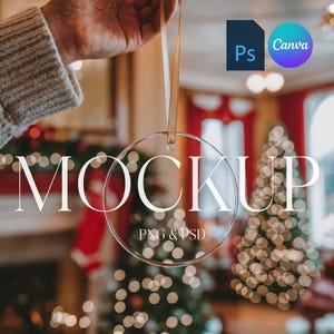 May include: A clear round Christmas ornament mockup hanging from a gold ribbon. The ornament is in focus and the background is blurred, showing a Christmas tree with lights and a fireplace.