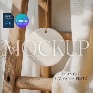 May include: A round, off-white ceramic ornament hangs from a gold string. The word "MOCKUP" is displayed in large, white letters. The background includes a wooden ladder, a white blanket, and the Canva and Photoshop logos.