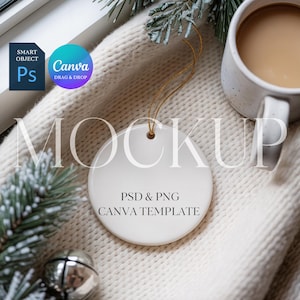 Może przedstawiać: Biała, okrągła ozdoba ceramiczna ze złotym sznurkiem, z tekstem "MOCKUP" i "PSD & PNG CANVA TEMPLATE". Ozdoba umieszczona jest na kremowym, dzianinowym kocu, z kubkiem kawy i dekoracyjnymi gałązkami sosny.