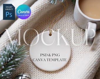 May include: A white ceramic round ornament with a gold string, featuring the text "MOCKUP" and "PSD & PNG CANVA TEMPLATE". The ornament is placed on a cream-colored knitted blanket, with a mug of coffee and decorative pine branches.