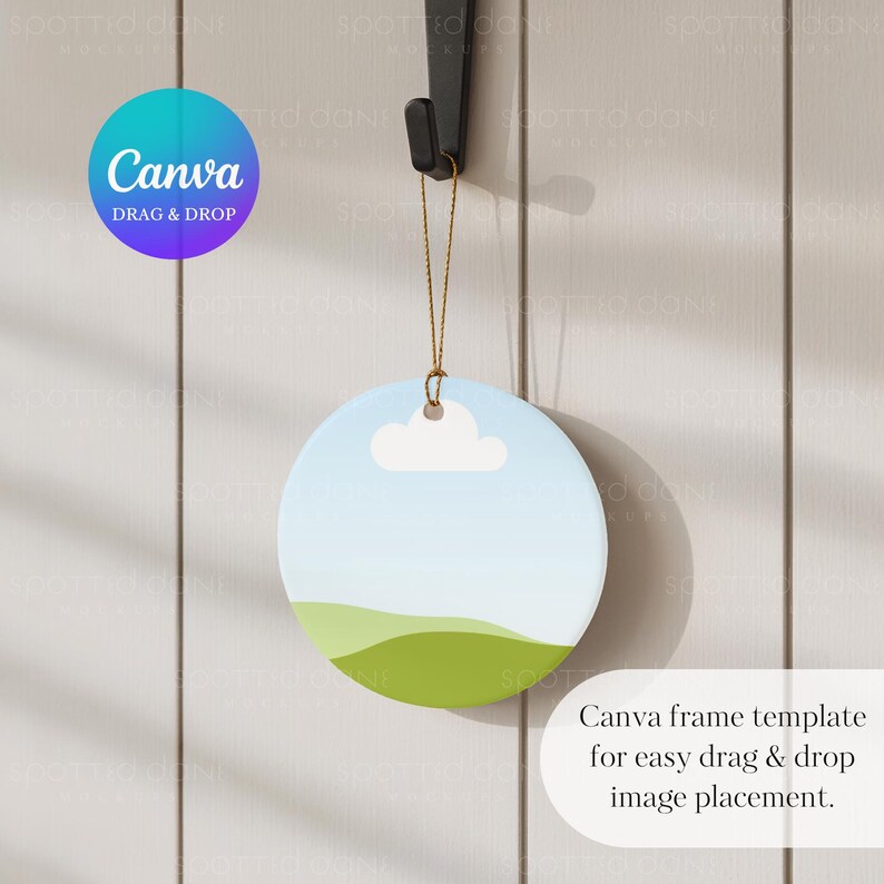 May include: A circular ceramic ornament with a sky and landscape design, suspended from a black hook. The ornament depicts a blue sky, a white cloud, and green hills. Text on the image says "Canva DRAG & DROP" and "Canva frame template for easy drag & drop image placement."