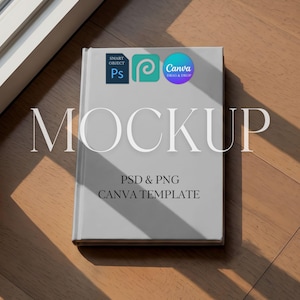 May include: A light gray book mockup with the word "MOCKUP" in large white letters. The book has three small circular logos and the text "PSD & PNG CANVA TEMPLATE" below the word "MOCKUP". The book is on a wooden surface.