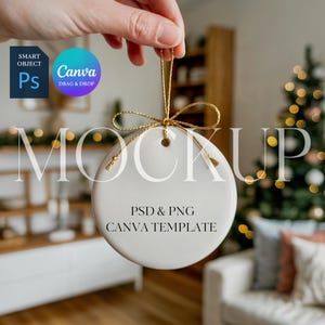 May include: A white, round Christmas ornament with a gold string and bow is held up. The ornament has the word "MOCKUP" in large letters across the front, with the text "PSD & PNG CANVA TEMPLATE" below. A Christmas tree with lights is in the background.