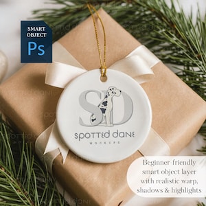May include: A white ceramic ornament with a gold string, featuring a Dalmatian dog design and the text "Spotted Dane Mockups." The ornament is on a wrapped gift with a cream ribbon and evergreen sprigs.