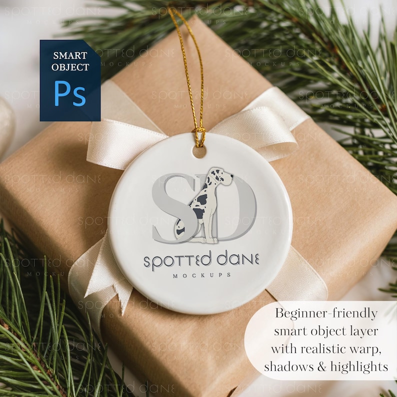 May include: A white ceramic ornament with a gold string, featuring a Dalmatian dog design and the text "Spotted Dane Mockups." The ornament is on a wrapped gift with a cream ribbon and evergreen sprigs.