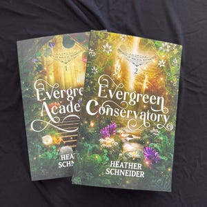 May include: Two hardcover books titled "Evergreen Academy" and "Evergreen Conservatory" by Heather Schneider. The covers feature a lush, green botanical design with floral accents and the text "Society of Magical Botanists". The books are set against a black background.