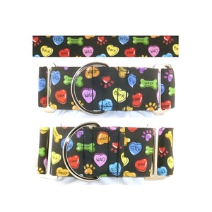 May include: Black dog collar with a repeating pattern of colorful hearts, paw prints, and bone shapes. The hearts have words like "FETCH", "WAG", and "BARK". The collar has a silver metal D-ring and side release buckle.