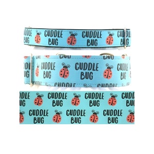 Puede incluir: Tres collares para perros con un fondo azul claro. Los collares presentan las palabras "CUDDLE BUG" y un gráfico de mariquita. Los collares están hechos de un material duradero y tienen herrajes metálicos.