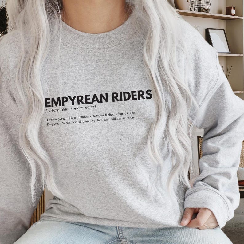 K&ouml;nnte beinhalten: Hellgraues Sweatshirt mit schwarzem Text "EMPYREAN RIDERS" und Definition. Das Sweatshirt besteht aus einem weichen Material. Der Text darunter besagt, dass die Empyrean Riders-Fangemeinde Rebecca Yarros und die Empyrean-Serie feiert, mit Fokus auf Liebe, Verlust und Milit&auml;rluftfahrt.