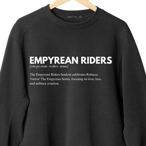 K&ouml;nnte beinhalten: Schwarzes Sweatshirt mit dem wei&szlig;en Text "EMPYREAN RIDERS", einer Definition und einer Beschreibung der Fangemeinde. Das Sweatshirt h&auml;ngt an einem Holzkleiderb&uuml;gel.