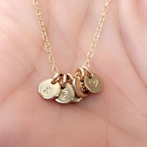 May include: A gold chain necklace with five small gold charms. The charms are round and have letters and a heart engraved on them.