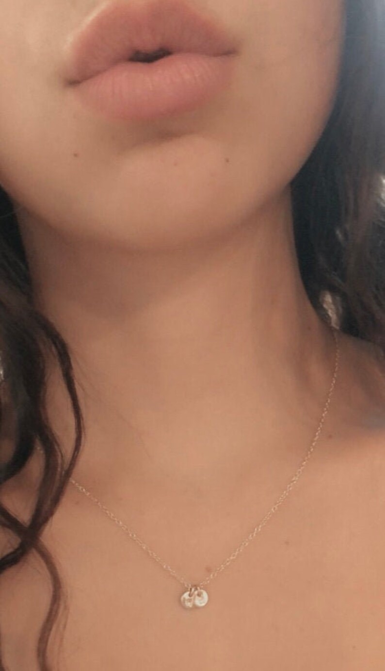 May include: A close-up of a person's neck wearing a delicate gold chain necklace with a small, round pendant.