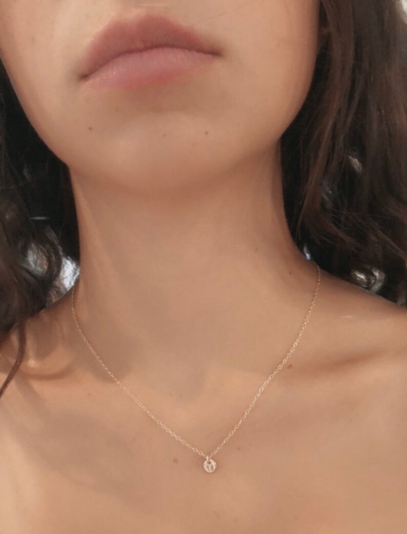 May include: A delicate gold chain necklace with a small, round pendant. The pendant appears to be a simple, minimalist design.
