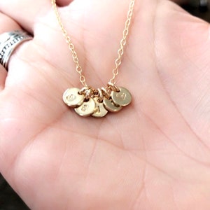 May include: A gold necklace with multiple small round charms, each with a letter engraved on it.