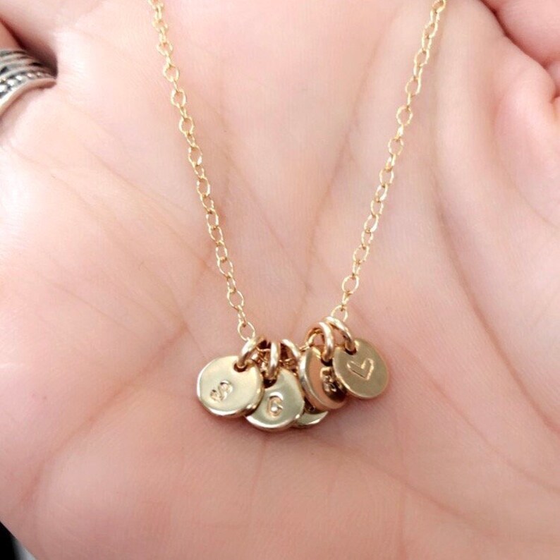 May include: A gold chain necklace with five small gold charms. The charms are round and have letters and a heart engraved on them.
