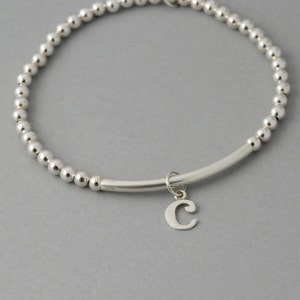 May include: A silver beaded bracelet with a silver bar and a silver charm with the letter C.