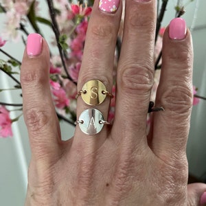 May include: Two gold and silver rings with initial charms. The gold ring has the letter "S" and the silver ring has the letter "A".