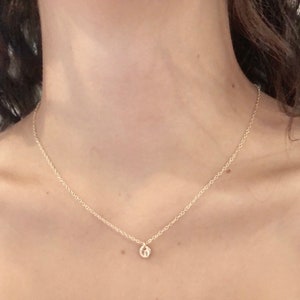 May include: A delicate gold chain necklace with a small, round pendant. The pendant is a simple, minimalist design.