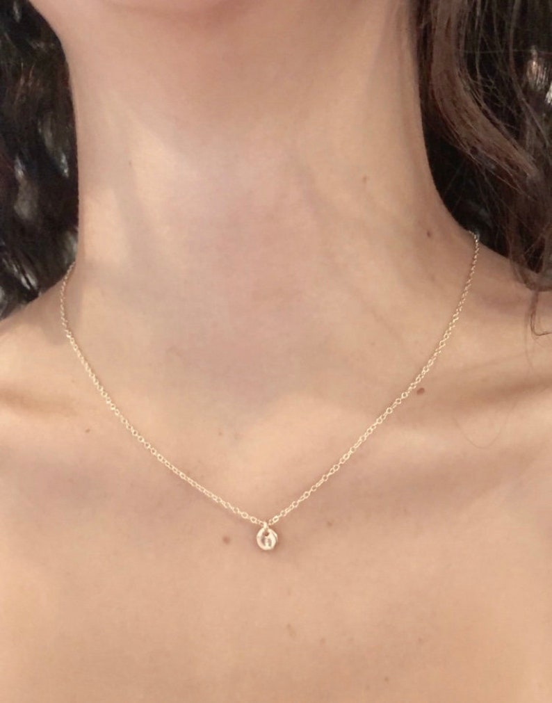 May include: A delicate gold chain necklace with a small, round pendant. The pendant is a simple, minimalist design.