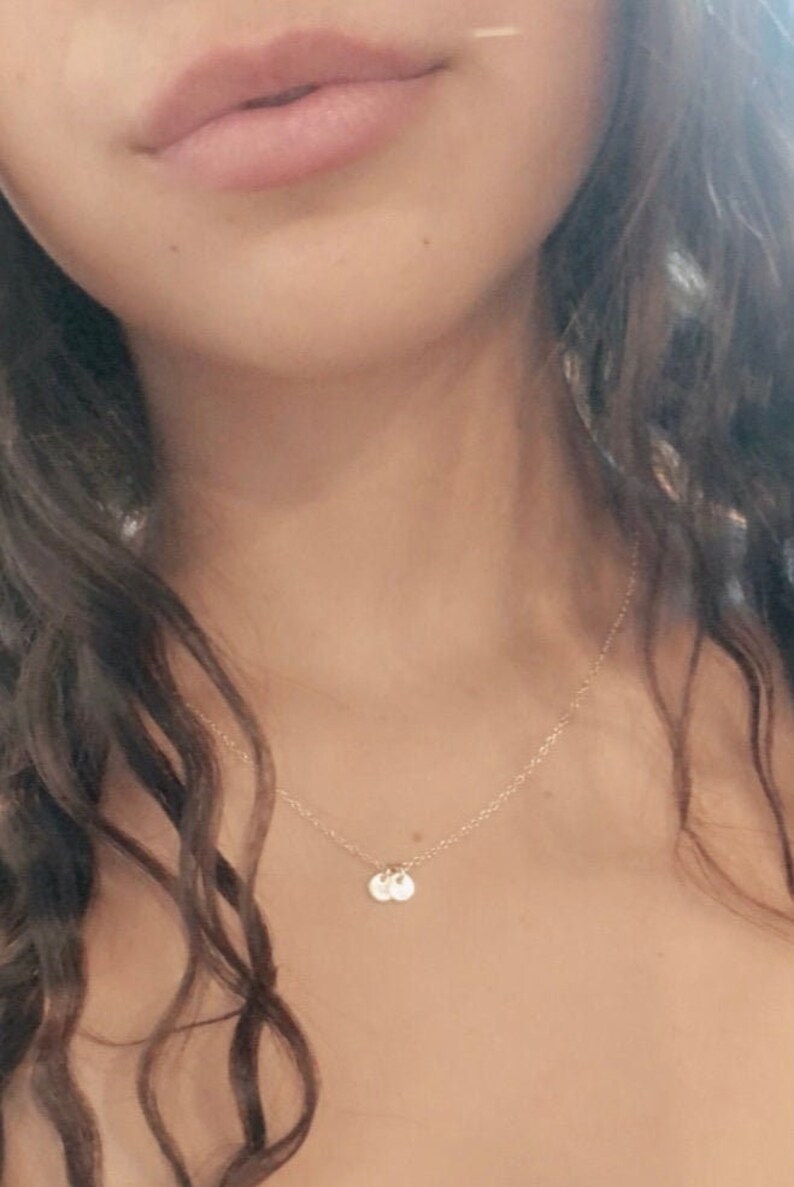 May include: A close-up of a person wearing a delicate gold necklace with two small, round pendants. The necklace is simple and elegant, and the pendants are barely visible.