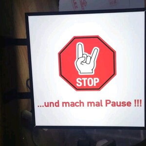 Puede incluir: Un letrero blanco con marco negro y una señal de stop roja con una mano haciendo el signo de rock and roll. El texto en el letrero dice "...und mach mal Pause!!!"