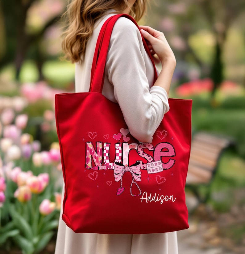 May include: A red tote bag with the word "NURSE" in a pink and white design, with hearts and a stethoscope graphic. The name "Addison" is printed below the graphic. The bag has red handles.