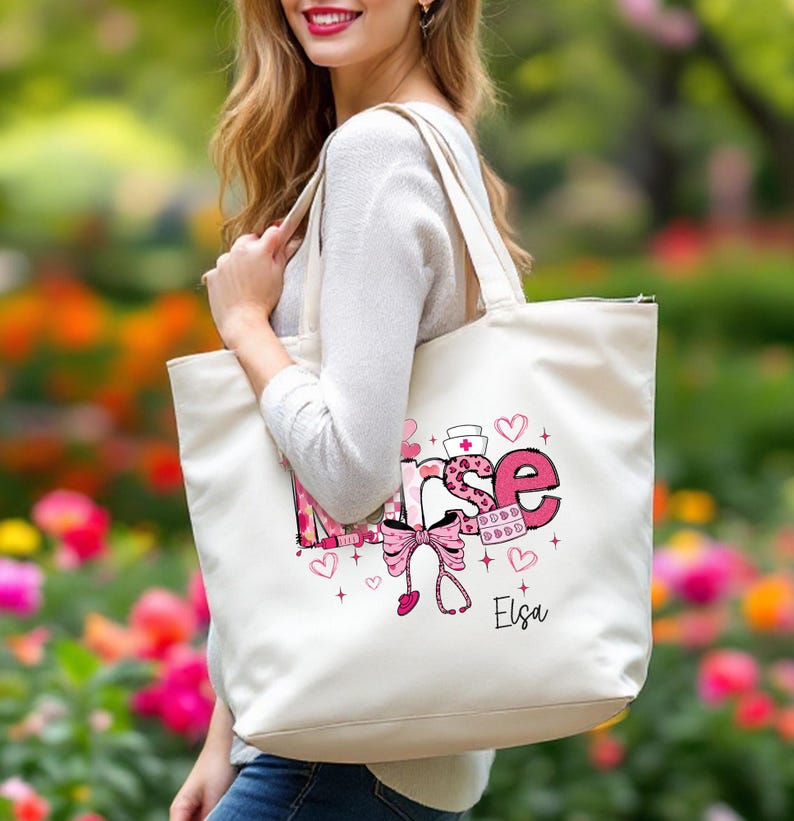 May include: Cream-colored tote bag with the word "Nurse" in pink and white, decorated with hearts, a stethoscope, and a bow. The bag has a name, "Elsa," printed in black. The bag is carried by a person.