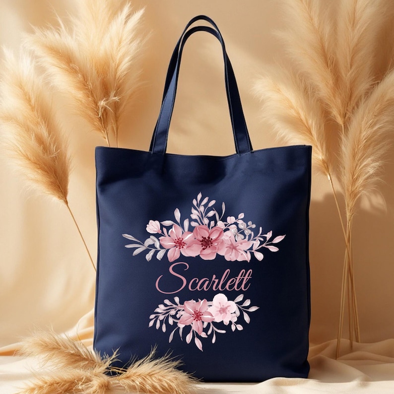 May include: A navy blue canvas tote bag with a floral design and the name "Scarlett" printed in pink.