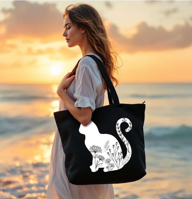 K&ouml;nnte beinhalten: Eine schwarze Tragetasche mit einer wei&szlig;en Silhouette einer Katze mit floralen Details. Die Tasche hat einen Rei&szlig;verschluss.