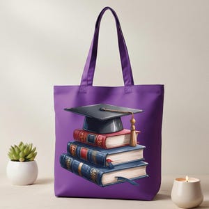 May include: A purple tote bag featuring a stack of books and a graduation cap. The books are red and blue with gold accents, and the cap is black with a gold tassel. The bag has a simple design, perfect for carrying books or other items.