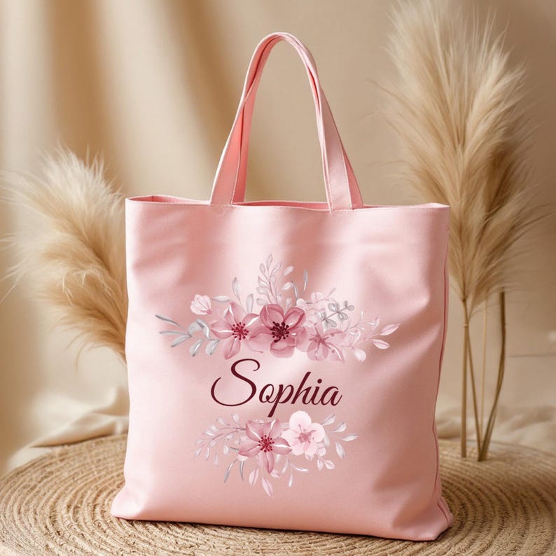 May include: A pink canvas tote bag with a floral design and the name "Sophia" printed in burgundy.