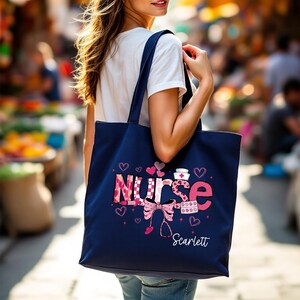 May include: A navy blue tote bag with the word "NURSE" in pink and patterned letters, decorated with hearts, a stethoscope, and a nurse's hat. The name "Scarlett" is printed below the design.