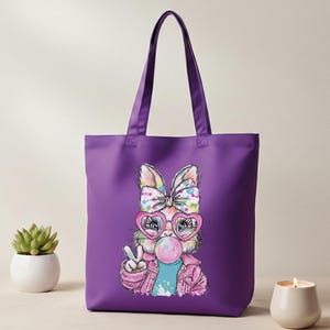 May include: A purple tote bag featuring a cartoon rabbit with a bow, heart-shaped glasses, and a bubble gum bubble. The rabbit is wearing a pink jacket and making a peace sign. The bag has two purple handles.