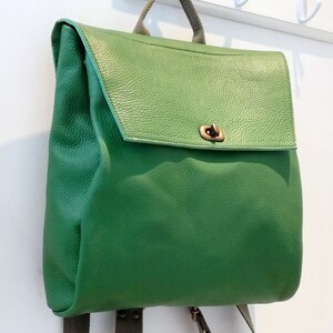 May include: A green leather backpack with a flap closure and a brass buckle. The backpack has adjustable straps and a small pocket on the front.