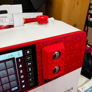 May include: A red sewing machine with a digital display screen and a BERNINA SPECIAL EDITION label. The machine has a red and white color scheme and features a variety of buttons and controls.