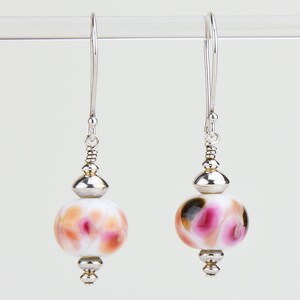May include: Silver dangle earrings with a white, pink, and brown glass bead. The bead has a swirl pattern.