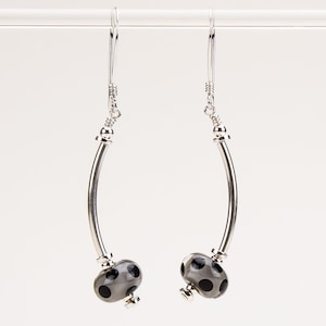 May include: Silver dangle earrings with a curved silver bar and a gray glass bead with black polka dots.