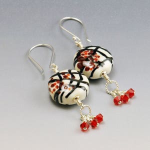 May include: A pair of silver dangle earrings with white and black patterned glass beads and red crystal accents.