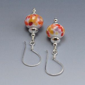 May include: A pair of silver dangle earrings with white glass beads. The beads are decorated with red, orange, and yellow spots.