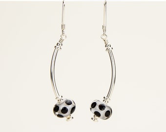 May include: A pair of silver earrings with a curved bar design and a black and white polka dot glass bead on each earring.