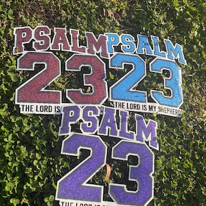 Może przedstawiać: Trzy znaki z tekstem "PSALM 23" i "THE LORD IS MY SHEPHERD". Cyfry i tekst są w kolorze bordowym, niebieskim i fioletowym z kropkowaną fakturą. Znaki znajdują się na zielonym listowiu.
