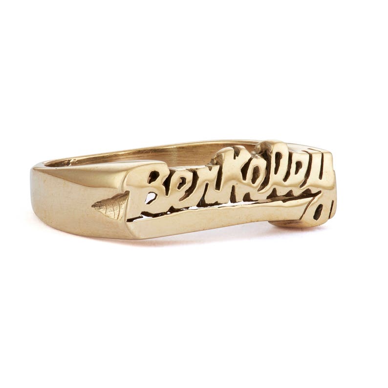 May include: A gold ring with the word "Berkeley" engraved in a stylized font.