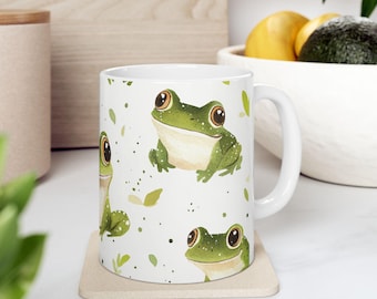 May include: White ceramic mug with a green frog pattern. The mug has a handle and is sitting on a beige coaster.