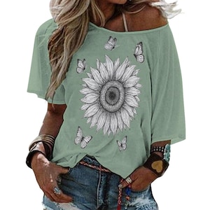 May include: Sage green off-the-shoulder top featuring a large black and white sunflower graphic. The shirt also has several small butterfly illustrations. The top is paired with blue denim shorts.