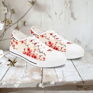 Könnte beinhalten: Weiße Canvas-Sneaker mit niedrigem Schaft und einem floralen Muster mit rosa Kirschblüten auf cremefarbenem Hintergrund.