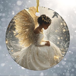 Op de afbeelding: Ronde kerstversiering met een engel in een witte jurk met gouden vleugels en een kroon. De engel staat tegen een besneeuwde bosachtergrond met sprankelende accenten. Een gouden draad is bevestigd om op te hangen.