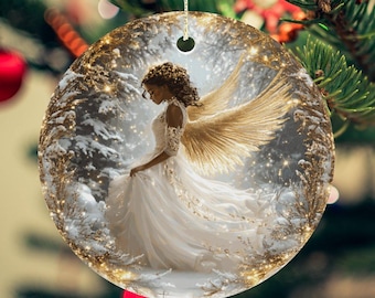 Puede incluir: Un adorno redondo de cerámica con un ángel blanco con alas doradas y un vestido blanco. El ángel está de pie en un bosque nevado con luces brillantes.