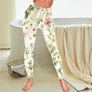 May include: Cream-colored leggings with a floral pattern featuring pink, purple, and yellow flowers, along with green leaves and stems. The leggings have a high waist and a comfortable fit, perfect for yoga or everyday wear.