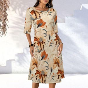May include: A cream-colored dress with a floral pattern in shades of orange, brown, and blue. The dress features a round neckline, elbow-length sleeves, and a knee-length skirt. The floral design is spread across the dress.
