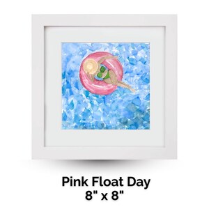 May include: Watercolor painting in a white frame depicts a person relaxing on a pink inflatable ring in blue water. The person wears a green swimsuit and a straw hat. The artwork is titled "Pink Float Day" and measures 8" x 8".